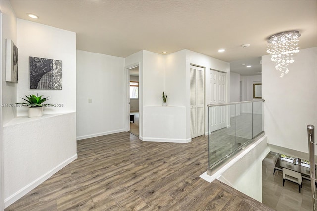 corridor with wood finished floors, baseboards, recessed lighting, an upstairs landing, and a chandelier