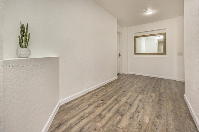 unfurnished room featuring wood finished floors, baseboards, and a textured wall