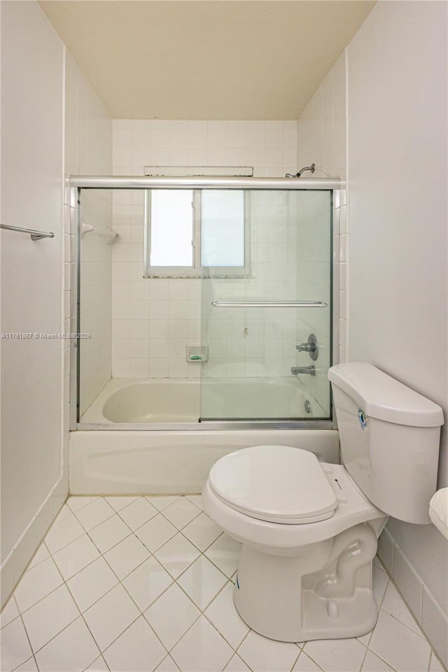 bathroom featuring baseboards, bath / shower combo with glass door, toilet, and tile patterned flooring