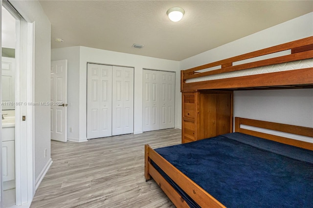 unfurnished bedroom with visible vents, two closets, a textured ceiling, light wood finished floors, and baseboards