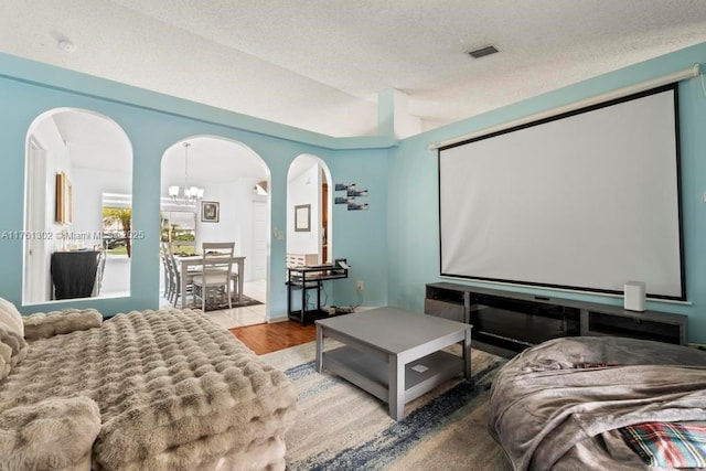 cinema room featuring wood finished floors, visible vents, an inviting chandelier, arched walkways, and a textured ceiling