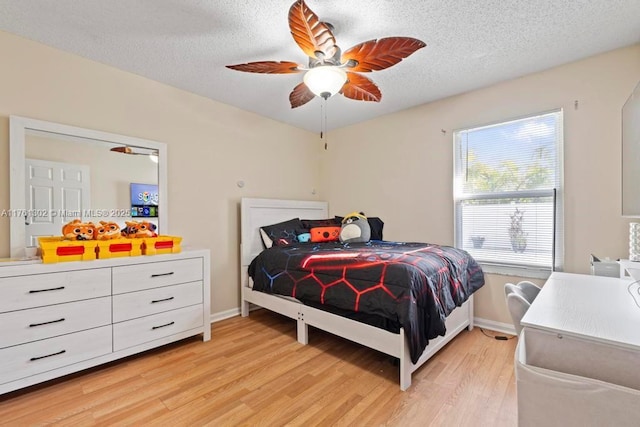 bedroom featuring ceiling fan, a textured ceiling, light wood-type flooring, and baseboards