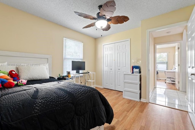 bedroom featuring light wood-type flooring, a textured ceiling, a closet, baseboards, and ceiling fan