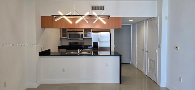 kitchen with dark countertops, appliances with stainless steel finishes, a peninsula, and a sink