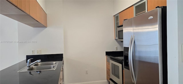 kitchen featuring dark countertops, stainless steel appliances, glass insert cabinets, and a sink