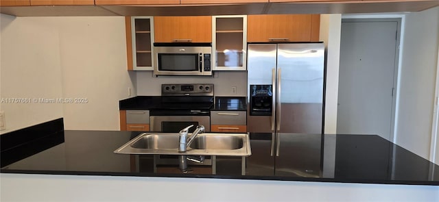 kitchen with a sink, glass insert cabinets, dark countertops, and appliances with stainless steel finishes