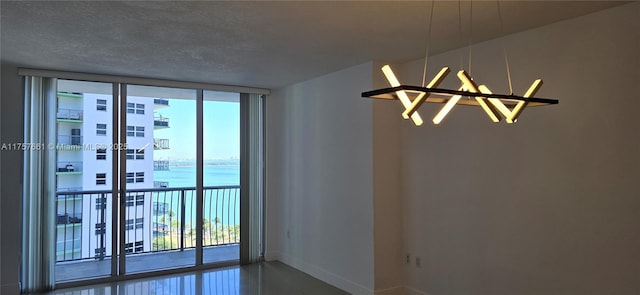 empty room with a water view, a notable chandelier, expansive windows, a textured ceiling, and baseboards