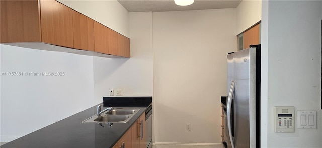 kitchen featuring dark countertops, brown cabinets, appliances with stainless steel finishes, and a sink