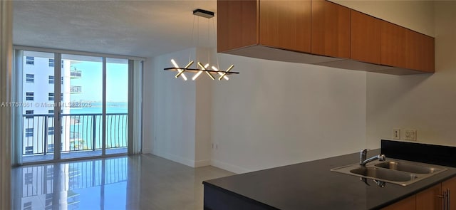 kitchen with dark countertops, baseboards, a wall of windows, brown cabinets, and a sink