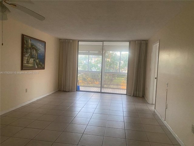 tiled spare room featuring expansive windows, baseboards, and a ceiling fan