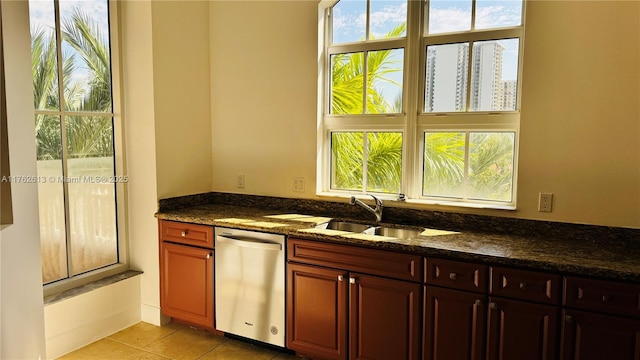 kitchen with a sink, dark stone counters, stainless steel dishwasher, and light tile patterned flooring