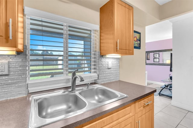 kitchen featuring a sink, backsplash, dark countertops, light tile patterned floors, and baseboards