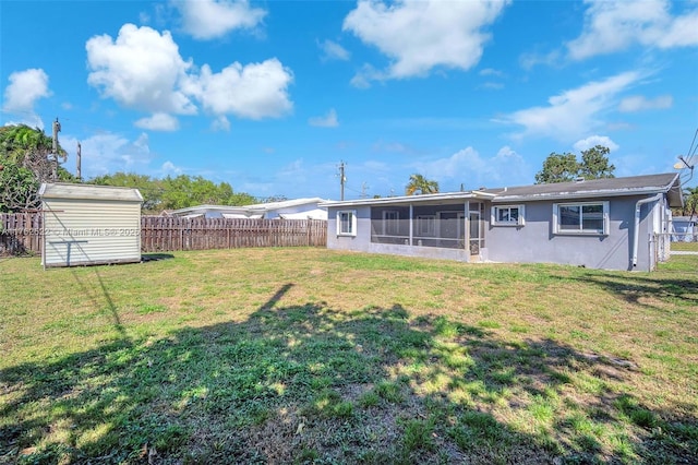 rear view of property featuring an outbuilding, fence, a sunroom, a storage unit, and a lawn