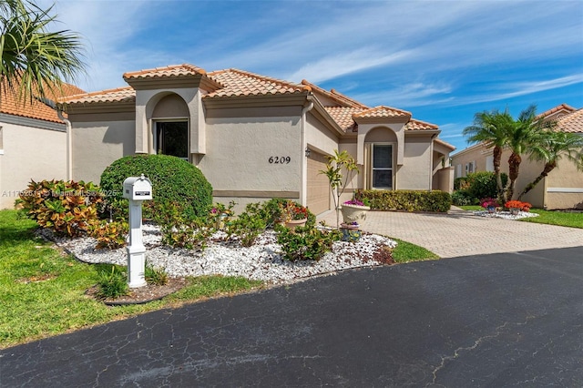 mediterranean / spanish house with a tiled roof, decorative driveway, a garage, and stucco siding