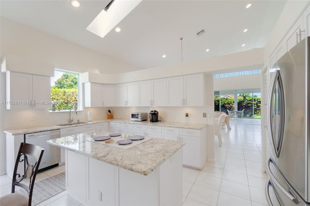 kitchen featuring a sink, a center island, stainless steel appliances, a skylight, and white cabinets