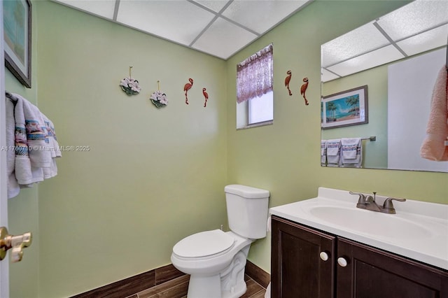 half bathroom with wood finish floors, a drop ceiling, toilet, and vanity