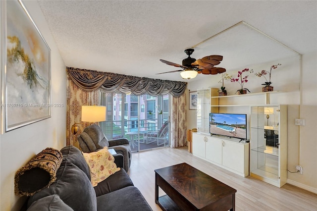 living room featuring light wood finished floors, baseboards, a textured ceiling, and ceiling fan