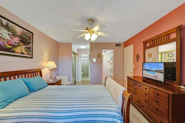 bedroom featuring ensuite bath, visible vents, a textured ceiling, and ceiling fan