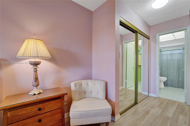 sitting room featuring baseboards, light wood finished floors, and a textured ceiling