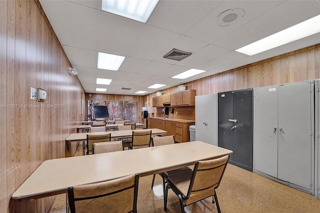 dining space featuring a drop ceiling, visible vents, and wood walls