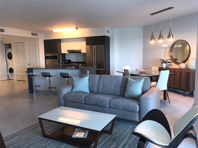 living area featuring visible vents, stacked washer and clothes dryer, and concrete floors