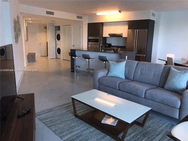 living area with visible vents, stacked washer and dryer, and marble finish floor