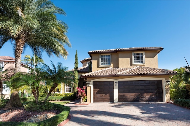 mediterranean / spanish home featuring stucco siding, decorative driveway, an attached garage, and a tiled roof