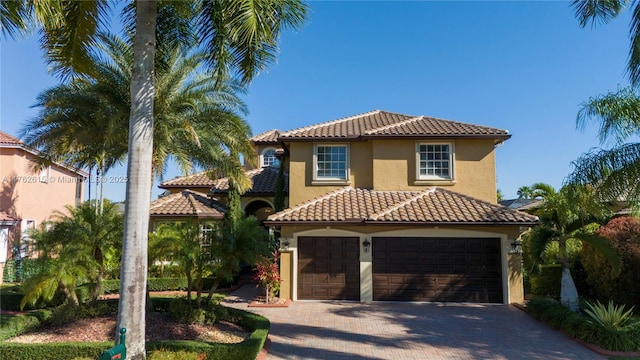 mediterranean / spanish home with stucco siding, decorative driveway, an attached garage, and a tiled roof