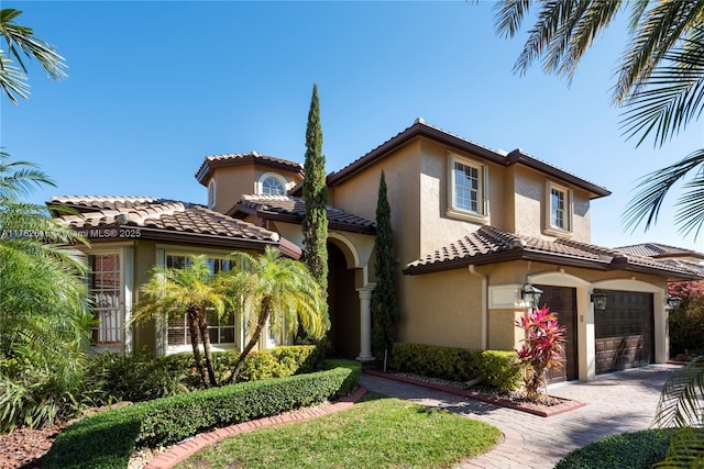 mediterranean / spanish home with a tile roof, decorative driveway, an attached garage, and stucco siding