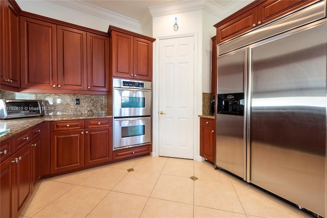 kitchen with tasteful backsplash, dark stone counters, appliances with stainless steel finishes, crown molding, and light tile patterned floors