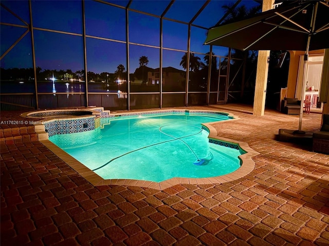 pool at night with glass enclosure, a pool with connected hot tub, and a patio area