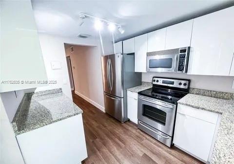 kitchen with white cabinets, appliances with stainless steel finishes, dark wood-type flooring, and light stone countertops