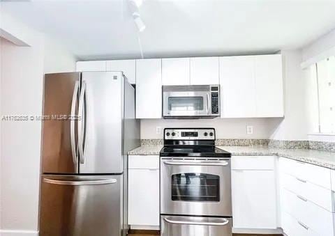 kitchen with light stone counters, white cabinetry, and stainless steel appliances