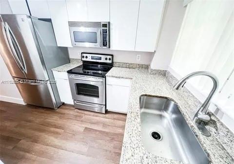 kitchen with light stone counters, wood finished floors, a sink, stainless steel appliances, and white cabinets