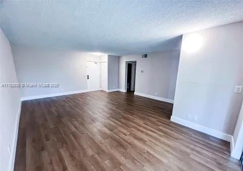 spare room featuring visible vents, a textured ceiling, dark wood-type flooring, and baseboards