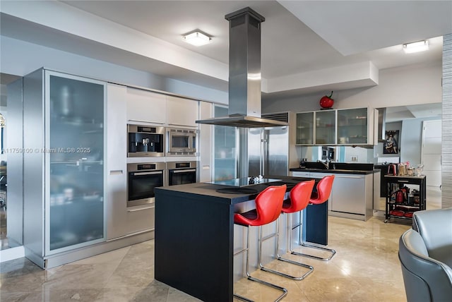 kitchen featuring island range hood, glass insert cabinets, built in appliances, dark countertops, and a center island