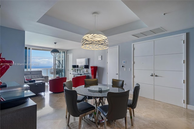 dining space featuring a tray ceiling, floor to ceiling windows, visible vents, and a water view