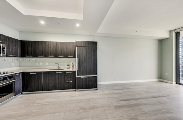 kitchen featuring baseboards, light countertops, stainless steel appliances, modern cabinets, and a sink