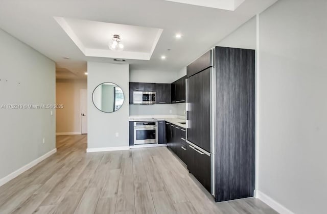 kitchen with light countertops, appliances with stainless steel finishes, a raised ceiling, modern cabinets, and light wood-type flooring