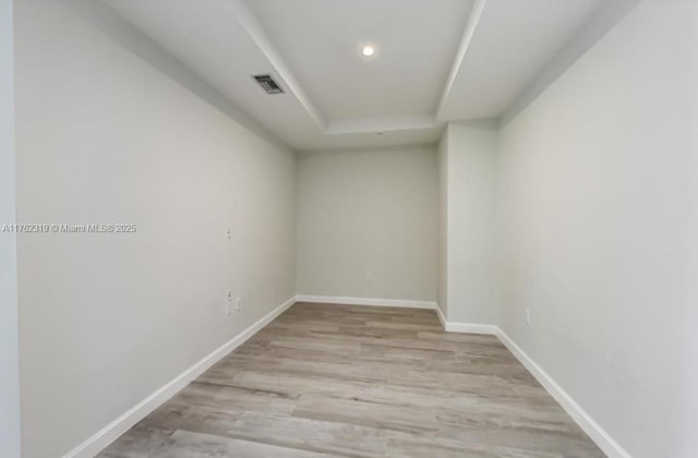 unfurnished room with visible vents, baseboards, a tray ceiling, light wood-style flooring, and recessed lighting