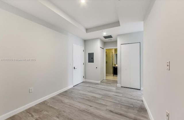 empty room featuring visible vents, electric panel, a tray ceiling, light wood-style floors, and baseboards