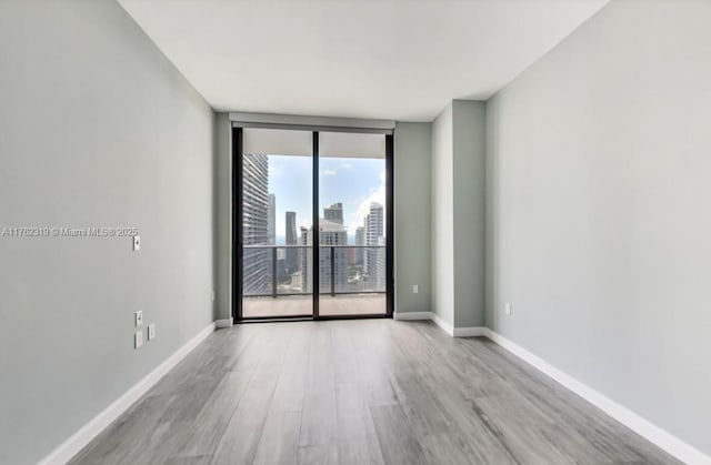 spare room featuring floor to ceiling windows, a view of city, baseboards, and wood finished floors