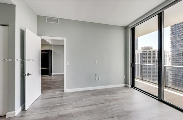 spare room with visible vents, wood finished floors, baseboards, and expansive windows