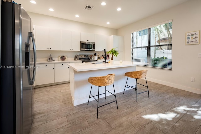 kitchen with a kitchen bar, visible vents, a sink, stainless steel appliances, and light countertops