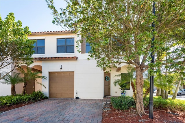 view of front of home with a tiled roof, decorative driveway, an attached garage, and stucco siding