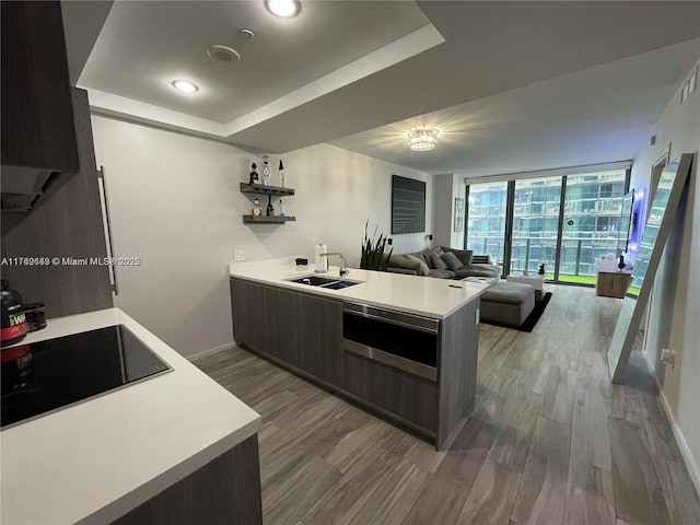 kitchen with a sink, floor to ceiling windows, a peninsula, light countertops, and black electric stovetop