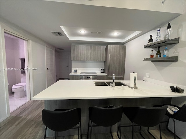 kitchen with a breakfast bar area, visible vents, a peninsula, a sink, and modern cabinets