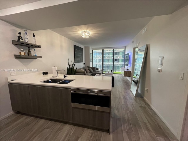 kitchen with dark wood finished floors, a wall of windows, a peninsula, and a sink