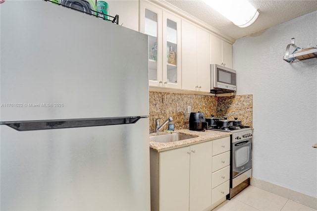 kitchen featuring stainless steel microwave, backsplash, range with gas cooktop, freestanding refrigerator, and a sink