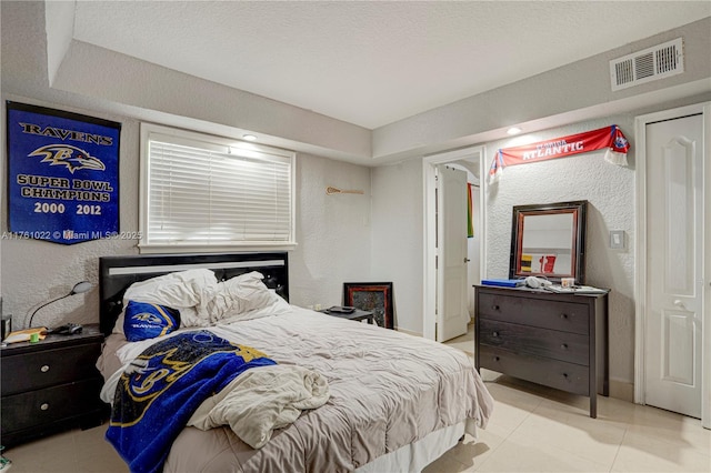 tiled bedroom with a textured wall, visible vents, and a textured ceiling